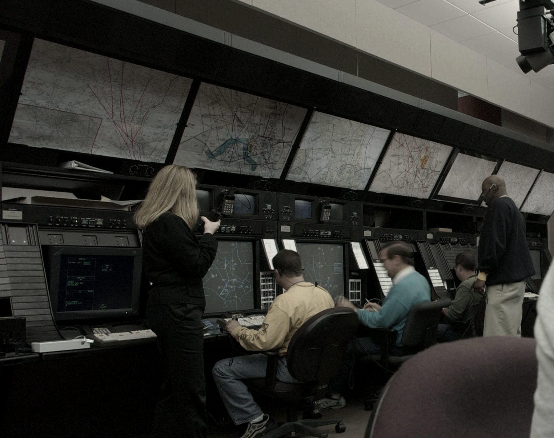 Controllers working radar positions beneath wall-mounted sectional charts on an operations floor