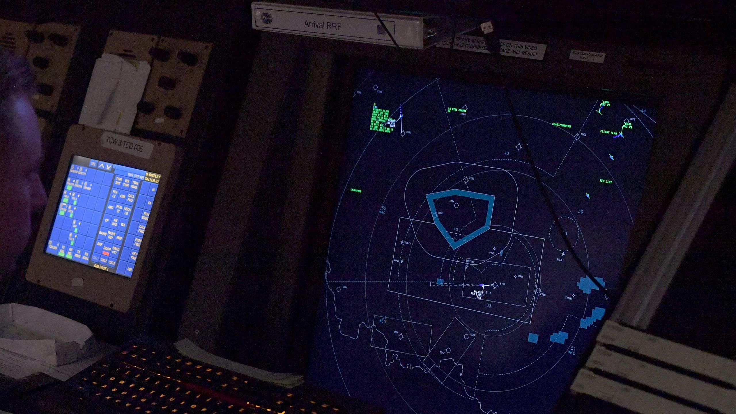 An air traffic control radar display showing tracked aircraft and airspace boundaries in a darkened facility